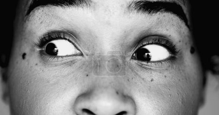 One scared young black woman macro close-up eyes looking directly at camera in SHOCK and HORROR feeling worry and paranoia to scary revelation, eye wide open