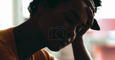 Foto de Mujer joven deprimida que sufre de enfermedad mental. Una persona negra abrumada por el estrés y la desesperación tranquila, cara cercana sosteniendo la cabeza con la mano - Imagen libre de derechos