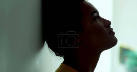 Foto de Una joven meditativa silueta de mujer negra de cerca en las sombras con una mirada pensativa reflexiva, el perfil de la joven persona afroamericana de 20 años - Imagen libre de derechos