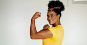 Happy Confident young African American woman showing strength, flexing arm looking at camera. One black latina shows muscle, we can do it symbol, wearing yellow shirt puzzle #716020282