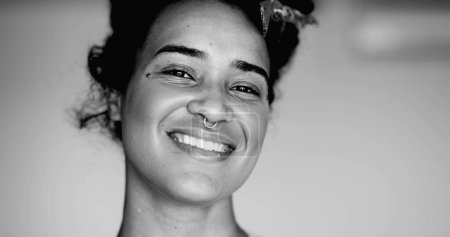 Téléchargez les photos : Heureuse latina noire d'origine africaine souriant à la caméra avec une expression amicale en noir et blanc Portrait monochromatique de la jeune femme brésilienne - en image libre de droit