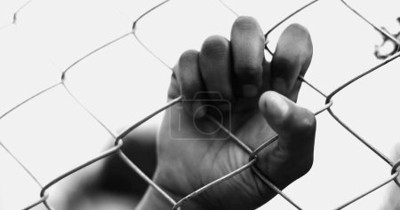 One Confined young black woman leaning on metal fence closing and opening eyes while hand holds on barrier tightly struggling in silence in dramatic monochrome, black and white