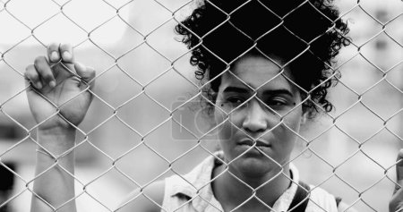 Téléchargez les photos : Une jeune femme noire piégée s'appuyant sur une clôture métallique urbaine dans un portrait monochromatique aux prises avec les défis de la vie, emprisonnée derrière une barrière. 20s personne souffrant - en image libre de droit