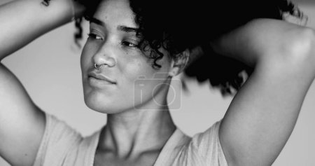 Foto de Joven brasileña negra latina de ascendencia africana juega con el peinado rizado en monocromático, blanco y negro. Retrato de una mujer de 20 años preparándose para ajustar el peinado - Imagen libre de derechos