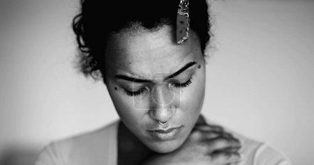 One preoccupied young black woman portrait feeling anxiety and worry during difficult times in dramatic black and white. Millennial person of African descent with pensive thoughtful emotion