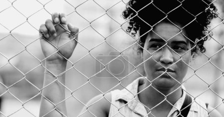 Foto de Una joven mujer negra atrapada apoyada en una valla metálica urbana en un retrato monocromático luchando con los desafíos de la vida, encarcelada detrás de una barrera. 20s persona que sufre - Imagen libre de derechos