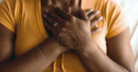 Téléchargez les photos : Jeune femme afro-américaine spirituelle mettre la main sur la poitrine ayant l'espoir et la foi. Une personne gestuelle réconfortante symbole de gratitude - en image libre de droit