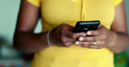 Photo for One young black woman using cellphone device standing up. African American 20s person holding phone engaged with modern technology - Royalty Free Image