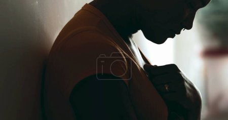 Photo for Young African American woman struggling during challenging times looking down with hands on chest seeking help and support in silhouette. Profile of a young black latina seeking help - Royalty Free Image