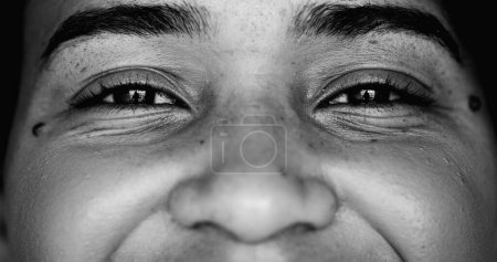 One young black woman smiling at camera, intense macro close-up detail person of African descent staring at camera with friendly happy demeanor in monochrome