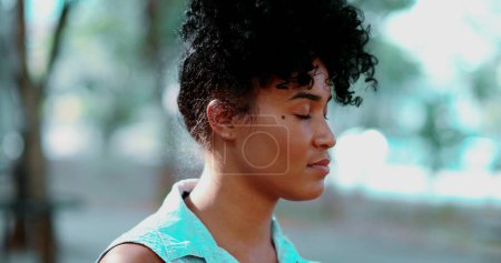 Téléchargez les photos : Portrait d'une jeune femme noire pensive debout en plein air dans un état de méditation paisible, le visage en gros plan dans le suivi des prises de vue pendant la journée ensoleillée et l'émotion contemplative - en image libre de droit