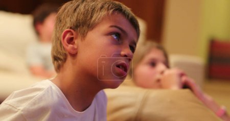 Foto de Niño joven cándido viendo la pantalla de televisión película vida real feliz reacciones infantiles auténticas - Imagen libre de derechos