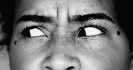 Photo for One paranoid worried young black woman macro close-up eyes looking sideways with intense preoccupation and obsession in dramatic black and white monochrome - Royalty Free Image