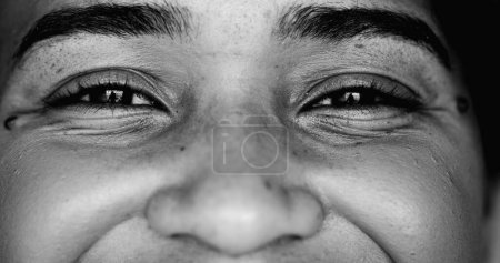 Photo for One young black woman smiling at camera, intense macro close-up detail person of African descent staring at camera with friendly happy demeanor in monochrome - Royalty Free Image