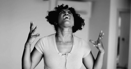 Joven mujer afroamericana estresada gritando de ira e incredulidad a dolorosa emoción desesperada y frustrada en dramático monocromo, blanco y negro