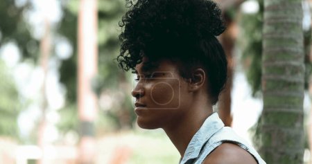 Foto de Una joven contemplativa de perfil negro cara de cerca en profunda reflexión mental sentada afuera en el parque con solemne emoción meditativa - Imagen libre de derechos