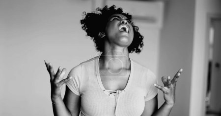 Joven mujer afroamericana estresada gritando de ira e incredulidad a dolorosa emoción desesperada y frustrada en dramático monocromo, blanco y negro