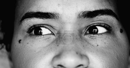 Photo for One paranoid worried young black woman macro close-up eyes looking sideways with intense preoccupation and obsession in dramatic black and white monochrome - Royalty Free Image