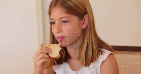 Téléchargez les photos : Candid enfant manger une collation sandwich et agitant voler loin avec la main - en image libre de droit