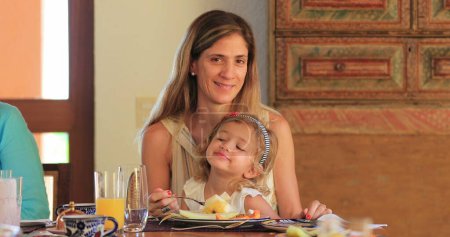 Téléchargez les photos : Adorable petite fille enfant avec mère manger table de déjeuner agissant mignon - en image libre de droit