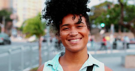 Photo for One happy young black woman of African Descent with curly hair standing in urban setting smiling. Portrait of a South American adult 20s girl - Royalty Free Image