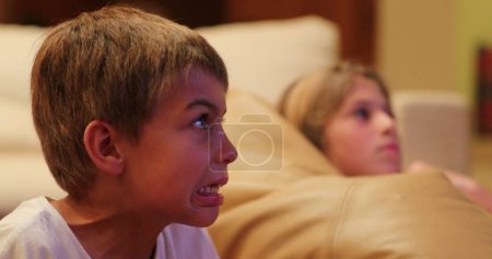 Téléchargez les photos : Réaction d'expression d'enfant devant l'écran de télévision la nuit réaction effrayante de jeune garçon - en image libre de droit