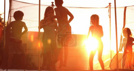 Téléchargez les photos : Enfants sautant à l'intérieur du trampoline à l'extérieur pendant l'heure dorée coucher de soleil enfants rebondissant avec éruption - en image libre de droit