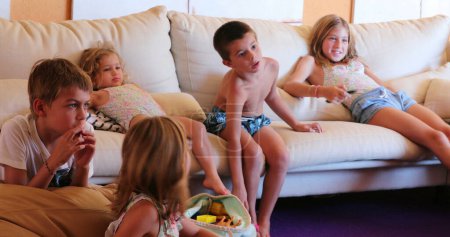 Téléchargez les photos : Beaucoup d'enfants assis un canapé salon regarder les enfants de la télévision ensemble à la salle de jeux - en image libre de droit