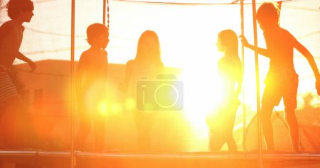 Photo for Children jumping inside trampoline outside during golden hour sunset time kids bouncing with flare - Royalty Free Image