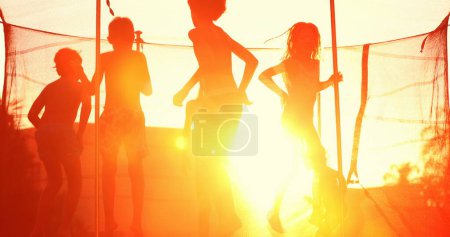 Foto de Niños saltando dentro del trampolín afuera durante la hora dorada del atardecer niños rebotando con bengalas - Imagen libre de derechos
