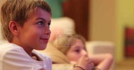 Foto de Niño frente a la pantalla de televisión viendo la película con reacciones auténticas de la vida real sonriendo al contenido - Imagen libre de derechos