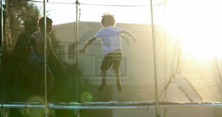 Foto de Niños saltando dentro de trampolín en un entorno al aire libre con lente resplandor sol brillante - Imagen libre de derechos