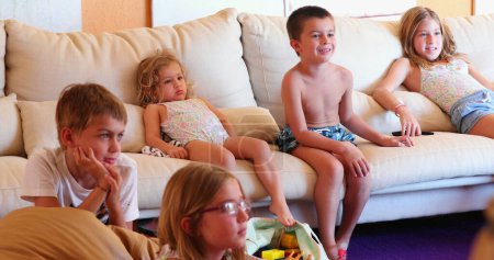 Téléchargez les photos : Enfants regardant l'écran de télévision ensemble assis sur le canapé du salon - en image libre de droit