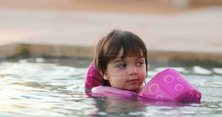 Kleines Mädchen im Wasser mit aufblasbaren Armen lernt