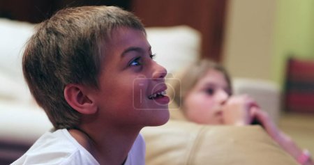 Photo for Young boy in front of tv screen watching movie with real life authentic reactions smiling to content - Royalty Free Image