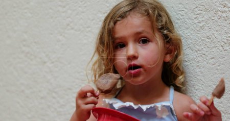 Téléchargez les photos : Candid small girl eating chocolate ice-cream - en image libre de droit