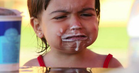 Téléchargez les photos : Petite fille bouleversée couverte de yaourt dans la bouche hochant la tête non - en image libre de droit