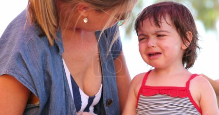 Foto de Cabreada niña niña llorando y quejándose madre abrazando hija calmante - Imagen libre de derechos