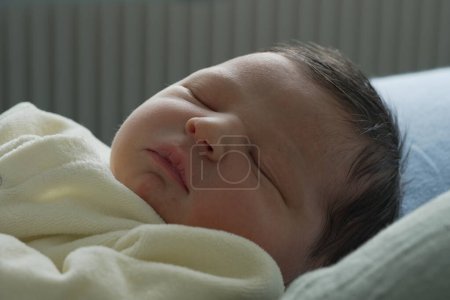 Téléchargez les photos : Un nouveau-né dans une onesie jaune doux dort paisiblement sur un oreiller bleu, avec de petites mains reposant doucement. Le gros plan capture la sérénité et l'innocence du bébé. - en image libre de droit