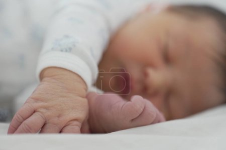 Das Baby schläft friedlich auf einer weißen Decke, wobei eine Hand ausgestreckt ist und die andere neben dem Gesicht ruht. Das weiche, natürliche Licht und der ruhige Ausdruck unterstreichen den ruhigen, erholsamen Moment.