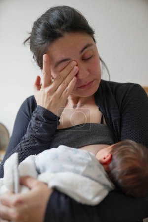 Eine neue Mutter wischt sich die Augen ab und hält ihr Baby während des Stillens fest, was die emotionale Tiefe und die körperlichen Anforderungen der frühen Mutterschaft veranschaulicht. Eine berührende Darstellung mütterlicher Liebe