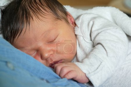 Photo for Close-up of a newborn baby sleeping peacefully on mother's chest, wrapped in a white blanket. The baby has soft, dark hair and a calm expression, highlighting the serenity of the moment - Royalty Free Image