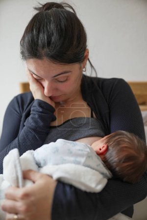 Erschöpfte Mutter, die ihr Baby mit geschlossenen Augen vor Müdigkeit wiegt, repräsentiert die emotionalen und physischen Anforderungen der frühen Mutterschaft. Dieses Bild fängt die tiefe Liebe und überwältigende Erschöpfung ein