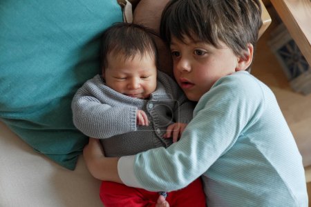 Hermano mayor acostado junto al bebé recién nacido, ambos mirando con calma. La luz suave y natural en la habitación mejora el vínculo entre hermanos pacíficos y amorosos