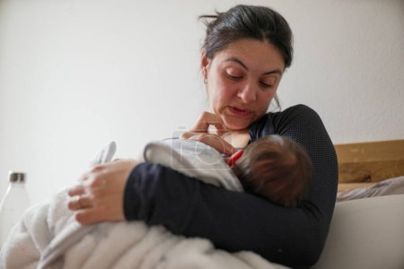 Madre amamantando a su recién nacido, ojos cerrados, mostrando las demandas emocionales y físicas de la maternidad temprana. Este tierno momento captura el vínculo y los desafíos experimentados en el posparto.