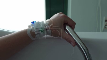 Main close-up avec IV goutte à goutte attachée tenant sur le support de rail métallique à l'intérieur de la baignoire, femme enceinte pendant le pré-travail