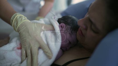 Nurse's hand trying to make newborn baby cry right after birth, infant's first seconds of life resting on mother's chest during childbirth moment, birthing of new life