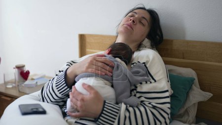 Tired mother sleeping with newborn baby on chest during first days of his life, exhausted mom sleeping laid in bed holding infant trying to rest during initial week