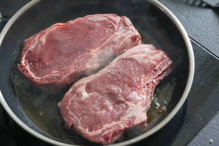 Téléchargez les photos : Ribeye steaks in a pan starting to sear, emphasizing the marbling and freshness of the meat, - en image libre de droit