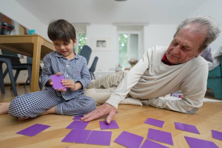 Young boy and elderly man enjoying a memory game on the floor, engaging in a playful and educational activity, indoor setting with bright natural light, highlighting family bonding and connection
